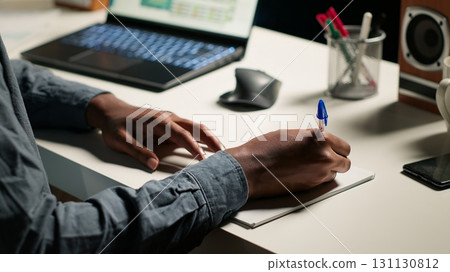 African American person working remotely and drafting project notes, organizing files and browsing web for relevant information. Comfortable home office setup for telework productivity. Camera B. 131130812