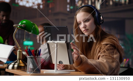 Young female adult listening to therapy music and working on her bachelor paper, using ambient sounds to help her focus in the university library. Student does academic research. Camera A. Young female adult listening to therapy music and working on her bachelor paper, using ambient sounds to help her focus in the university library. Student does academic research. Camera A. 131130950