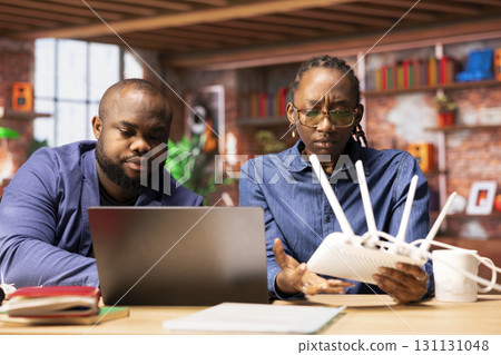 African american couple restarting their wireless router and checking network settings to resolve an internet error disrupting their freelance daily tasks. Signal loss during remote work. 131131048