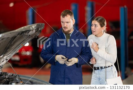 Mechanic checking young woman client car in car service center 131132170