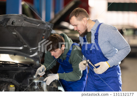Two mechanics fixing a broken car in a service station 131132177