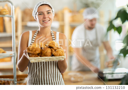 Female seller holds basket with finished products, shows many croissants 131132210