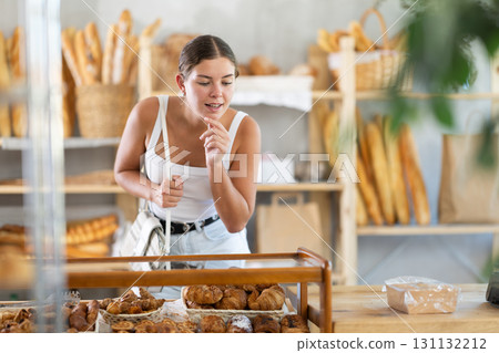 Young female customer chooses croissants in bakery 131132212