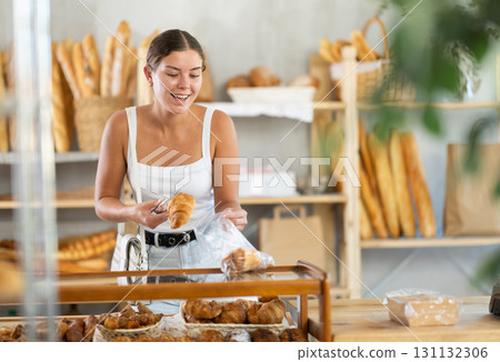 Young woman putting croissants in bag in bakery 131132306