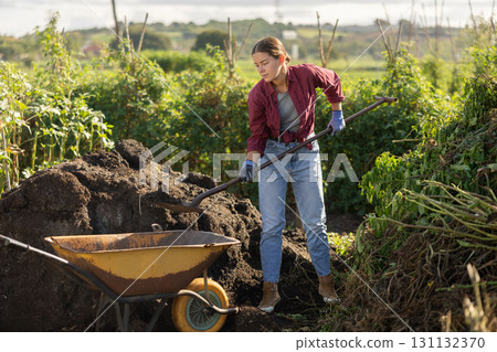 Woman puts black soil into a garden cart Woman puts black soil into a garden cart 131132370