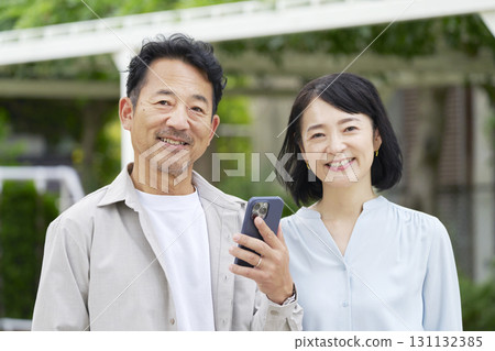 Middle-aged couple holding smartphones outdoors 131132385