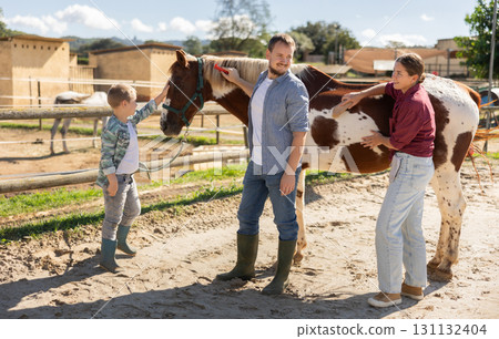 Man, woman and boy stroking and combing horse 131132404