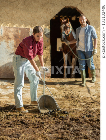 Young woman cleans manure near stable Young woman cleans manure near stable 131132406
