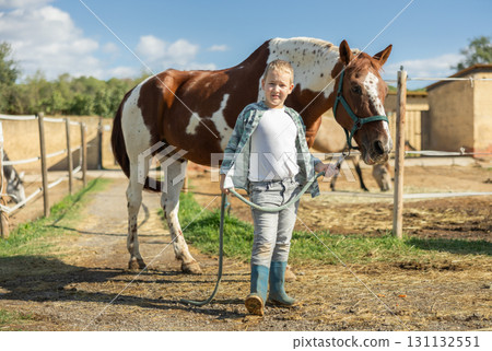 Happy boy leads a horse by the bridle for a walk in pasture Happy boy leads a horse by the bridle for a walk in pasture 131132551