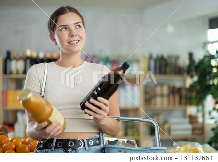 Girl hold packages bottles and choose consider juice in store 131132661