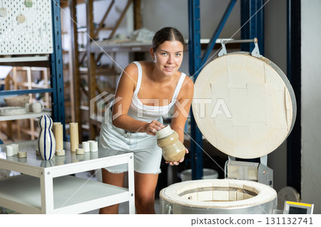 European girl in apron takes ready-made pottery made of clay out of oven 131132741