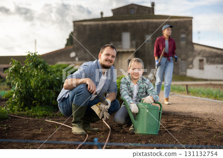 Young man with boy planting seeds in field 131132754