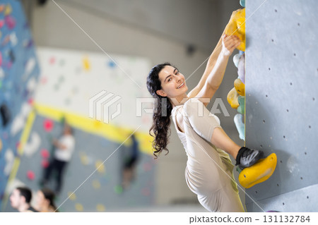 Motivated young girl climbing without ropes and harnesses on artificial bouldering wall in fitness center 131132784