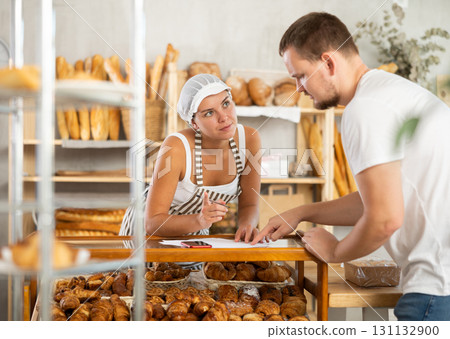 Young woman worker and a man write on sheets of paper by the croissants display Young woman worker and a man write on sheets of paper by the croissants display 131132900