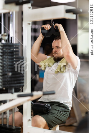 Man in gym performs exercises for arm muscles using cable crossover machine and pull weighted rope 131132918