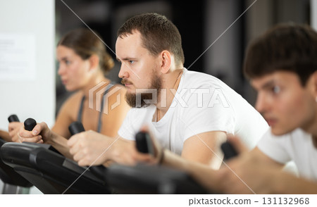Focused bearded man works out with stationary bicycle during class at fitness club 131132968