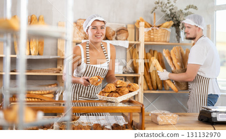 Young woman places croissants under the display while a man arranges baguettes on shelve 131132970