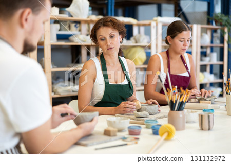 Three pottery workshop workers sculpt from raw clay 131132972