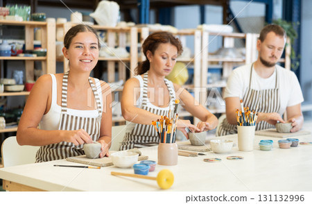 Three pottery workshop workers sculpt from raw clay 131132996