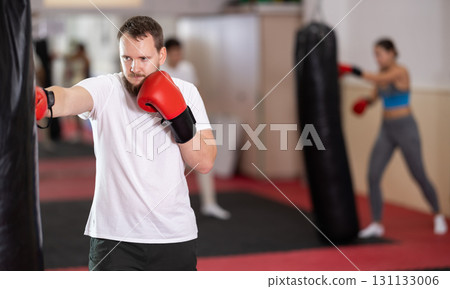 Bearded man punches and kicks punching bag in gym. Bearded man punches and kicks punching bag in gym. 131133006