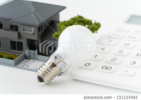 Close-up of a miniature detached house with a light bulb and a calculator 131133482