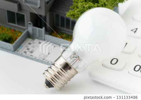 Close-up of a miniature detached house with a light bulb and a calculator 131133486