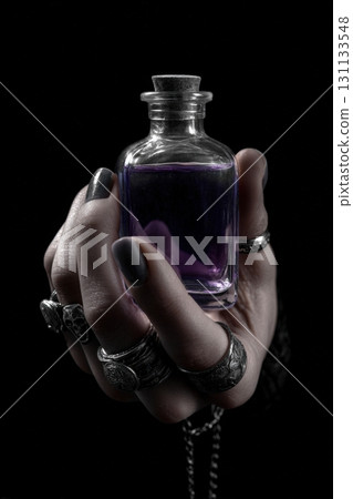 Hand with Silver Rings Holding Purple Potion Bottle on Black Background 131133548