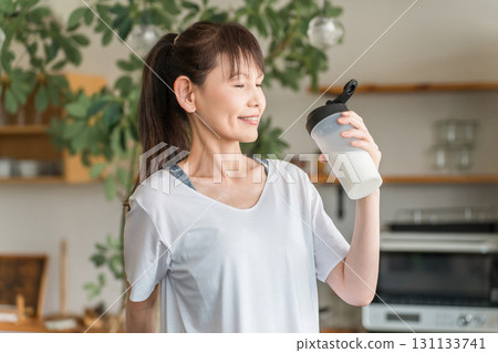 Asian woman drinking protein and EAA after training in the living room at home 131133741