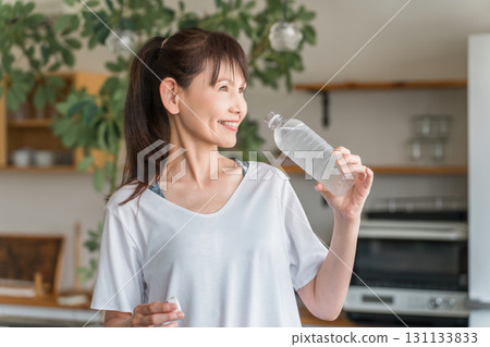 Asian woman hydrating with bottled mineral water after home training 131133833