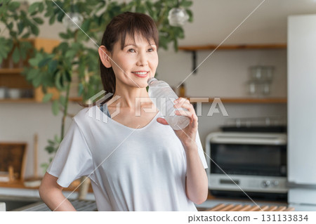 Asian woman hydrating with bottled mineral water after home training Asian woman hydrating with bottled mineral water after home training 131133834