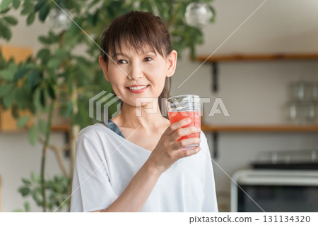 Young Asian woman drinking tomato juice, acerola, BCAA, red drink in front of her kitchen Young Asian woman drinking tomato juice, acerola, BCAA, red drink in front of her kitchen 131134320