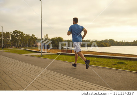 Sports guy runs through the city near the lake, back view 131134327