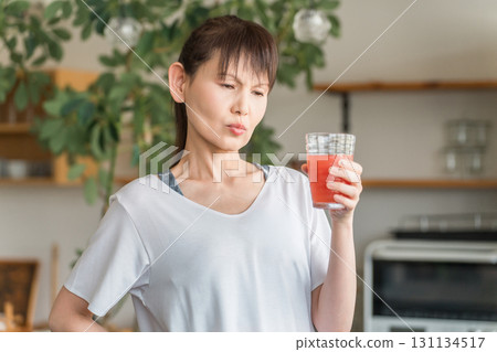Young Asian woman drinking tomato juice, acerola, BCAA, red drink in front of her kitchen 131134517