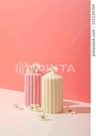 Two colorful candles sit on a pastel surface adorned with small flowers Two colorful candles sit on a pastel surface adorned with small flowers 131134704