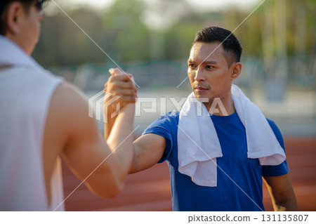 Close up of asian men joining hands and locking eyes with each other on racetrack in sports stadium. 131135807