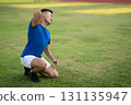 An asian man in blue t shirt touching his back while kneeling on the grass field. Pain or injury. 131135947