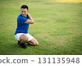 An asian man in blue t shirt is touching his shoulder while kneeling on grass field. Pain or injury. 131135948