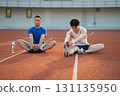 Two asian athlete men stretching their foots together, sitting on the racetrack in sports stadium. 131135950