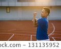 Asian man in blue t shirt is stretching his arm and shoulder muscles on racetrack in sports stadium. 131135952