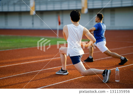 Two asian athlete men are stretching their muscles together on the racetrack in sports stadium. 131135956