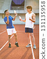 Two asian men are holding water bottles while talking together on the racetrack in sports stadium. 131135958