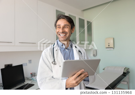 Happy smiling doctor standing in clinic office using digital pad 131135968