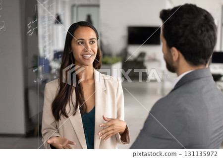Positive young business professional woman talking to coworker Positive young business professional woman talking to coworker 131135972