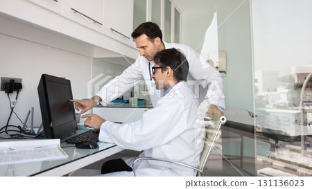 Busy male medical professionals share expertise at workplace by pc 131136023