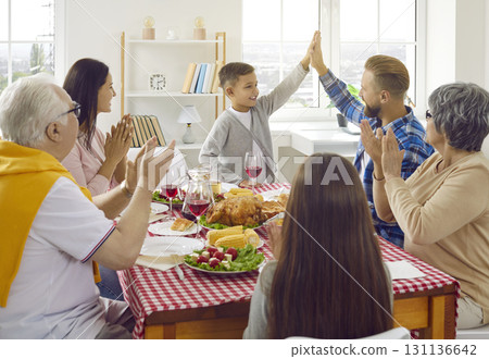 Joyful father and son give each other high five during family Thanksgiving dinner at home. Joyful father and son give each other high five during family Thanksgiving dinner at home. 131136642
