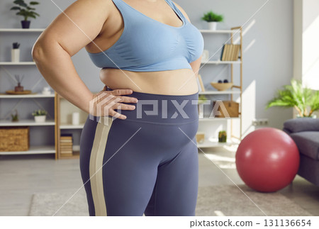 Cropped close up portrait of a belly and waist of fat overweight woman standing at home. Cropped close up portrait of a belly and waist of fat overweight woman standing at home. 131136654