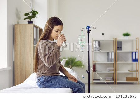 Child takes medicine with glass of water while getting medical IV line infusion at clinic 131136655