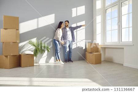 Loving husband and wife looking through window in their new home 131136667