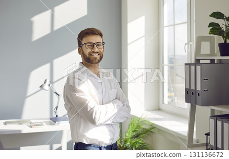 Businessman in white shirt standing in the office with crossed arms looking at camera and smiling. Businessman in white shirt standing in the office with crossed arms looking at camera and smiling. 131136672