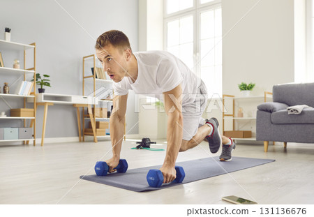 Motivated man doing a plank exercise with knee tucks during a fitness workout at home Motivated man doing a plank exercise with knee tucks during a fitness workout at home 131136676